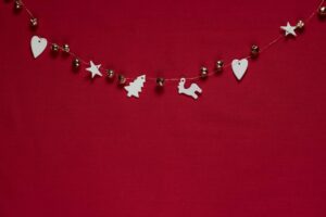 A simple white and silver holiday garland arranged methodically against a red background, featuring hearts, stars, a tree, and reindeer ornaments